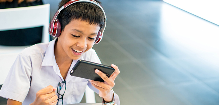 Photo of a boy with headphones watching a video on his cell phone