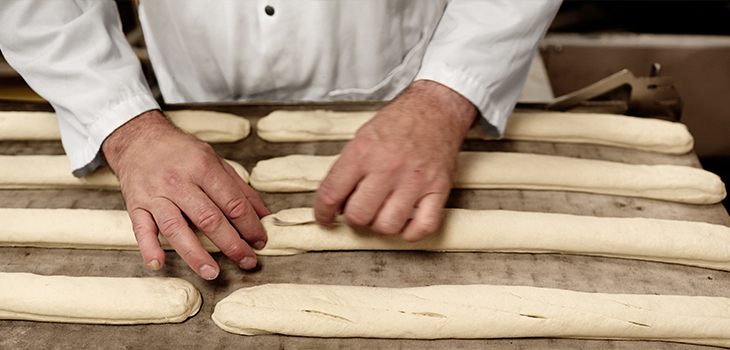 Photo de deux mains de boulanger alignant sur une plaque d’aluminium des pains pour la cuisson.