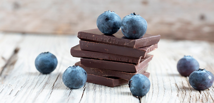 Photo conceptuelle : morceaux de chocolat empilés avec quelques bleuets sur une table en planche de bois.