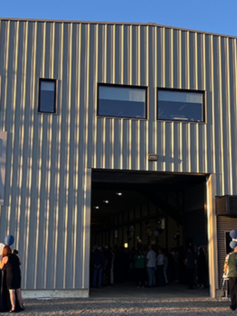 Façade d’une usine moderne en tôle métallique avec le logo « Acier DM » sur le mur, grande porte ouverte.