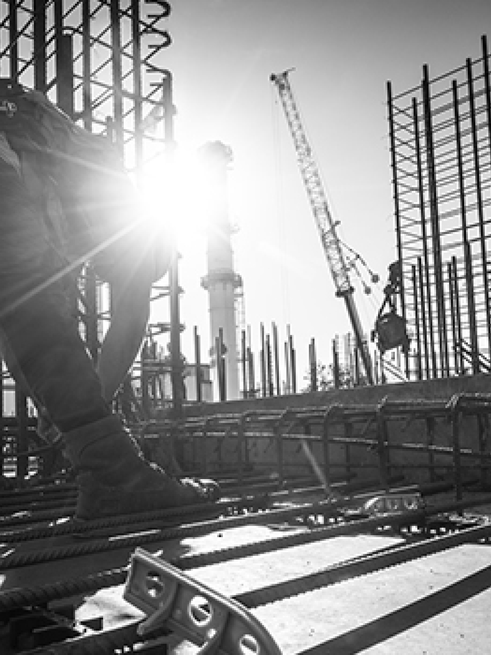 Travailleurs sur un chantier assemblant des barres d’armature en acier, avec le soleil en arrière‑plan et des structures verticales en construction.
