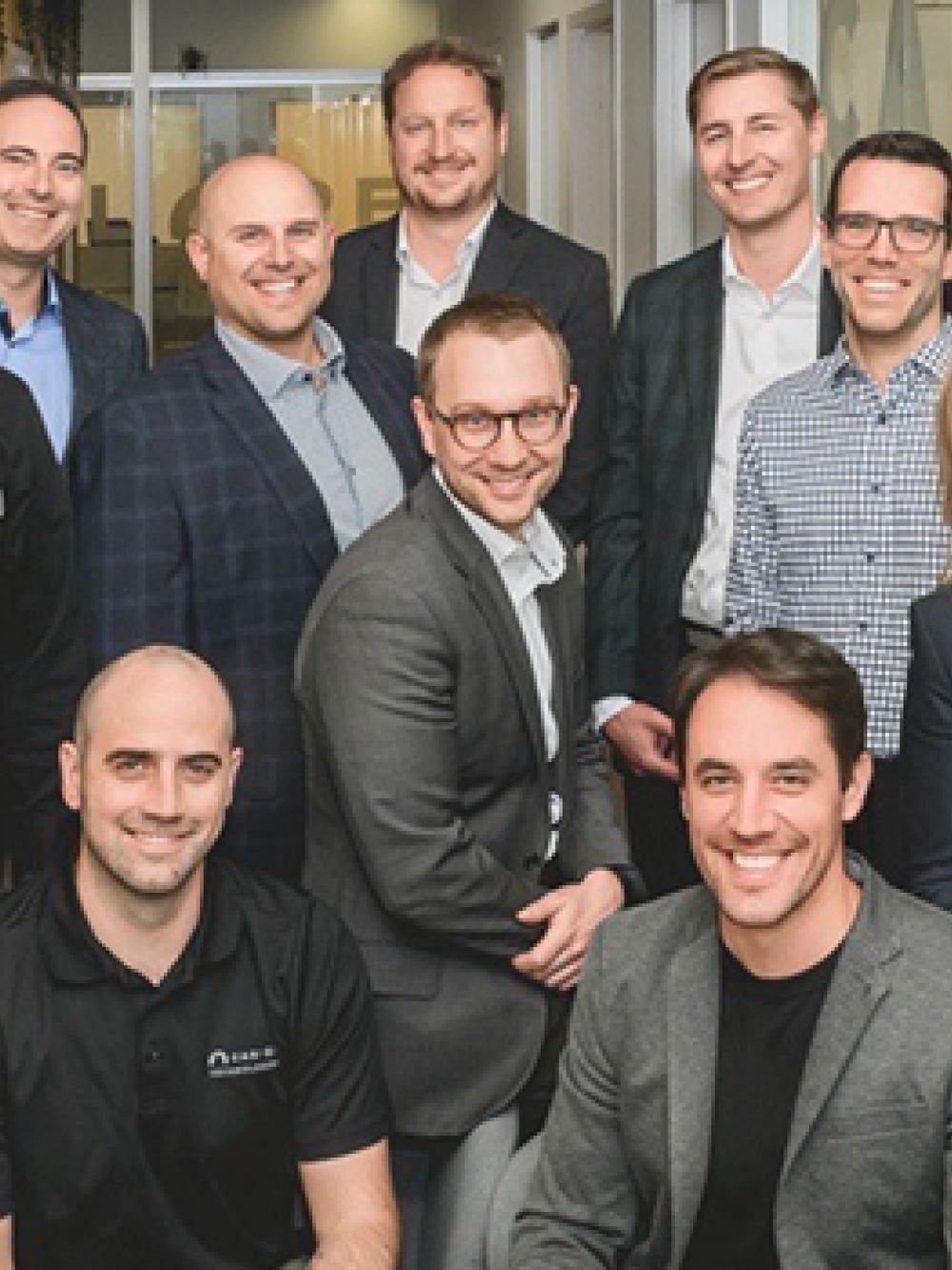 Groupe de personnes posant dans un bureau moderne, devant une paroi vitrée où l’on aperçoit une salle de réunion et des tableaux avec des notes.