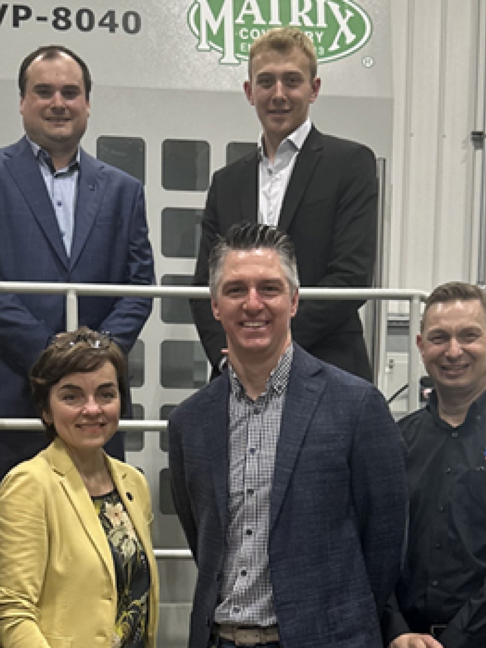 Groupe de personnes posant ensemble dans une usine devant un grand équipement industriel matricé, dans un environnement de production.
