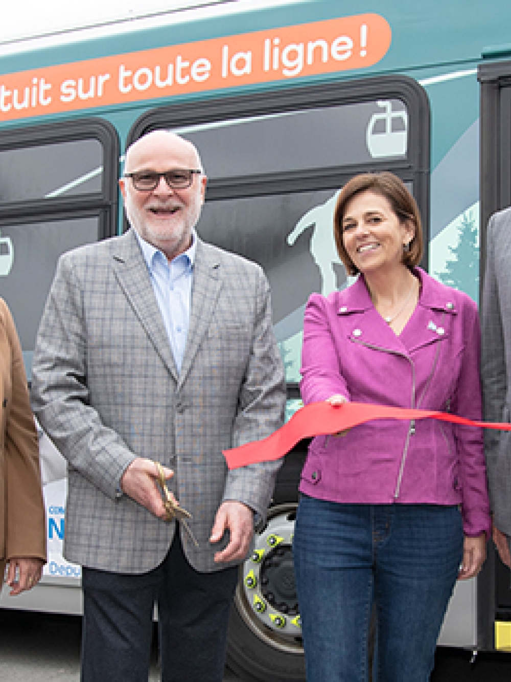 Groupe de personnes participant à une cérémonie d’inauguration devant un autobus, tenant un ruban rouge pour une coupe officielle.