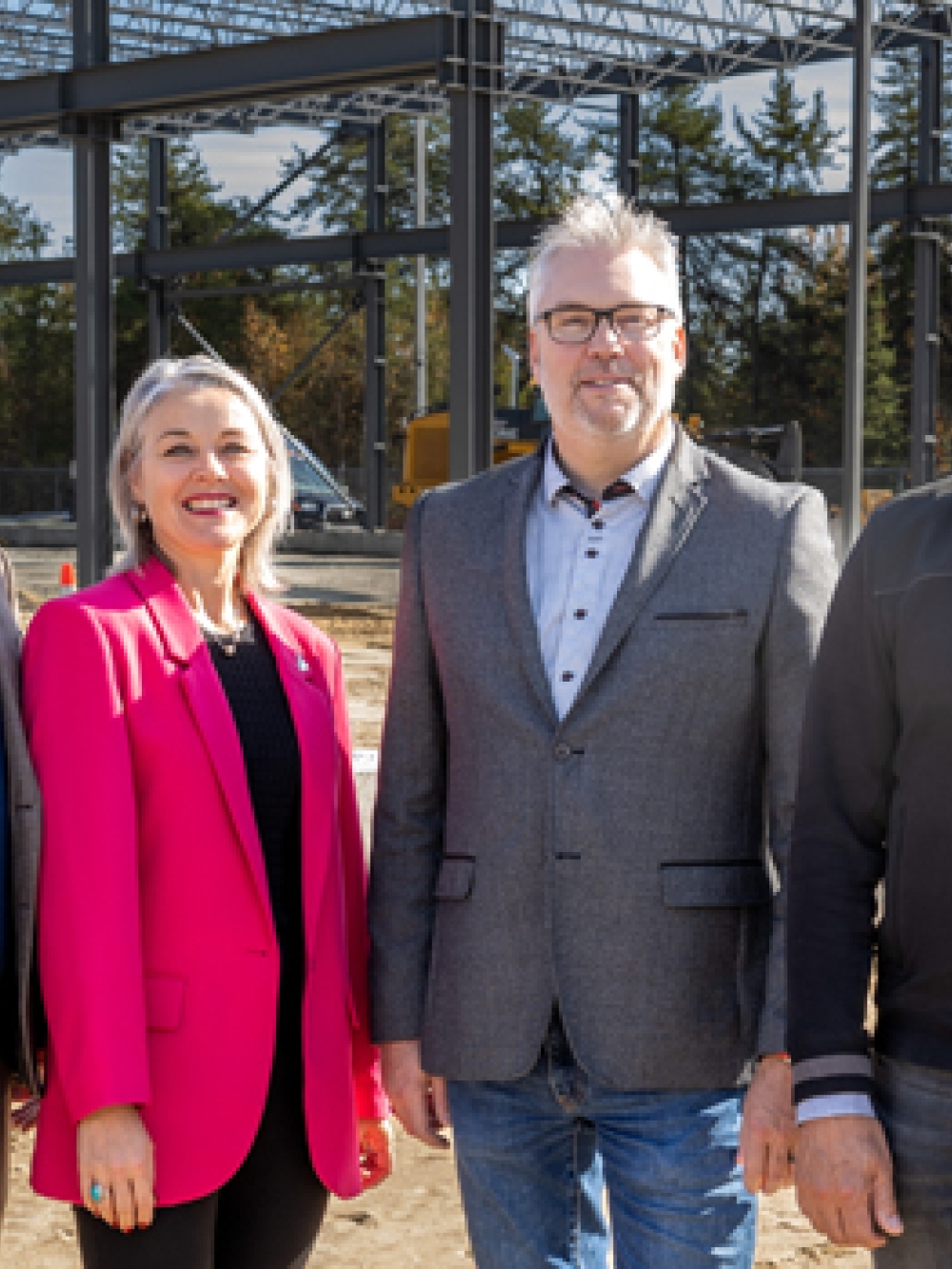 Groupe de personnes debout sur un chantier devant une structure métallique en construction, avec des poutres d’acier et des équipements de chantier visibles en arrière-plan.