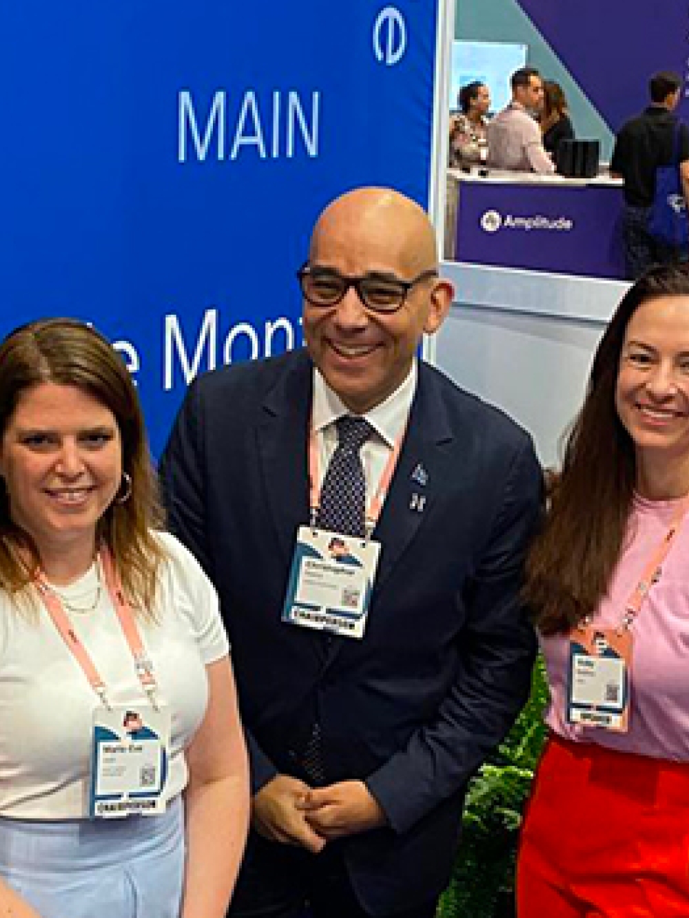 Cinq personnes debout à l’intérieur lors d’un événement professionnel, portant des badges autour du cou, devant un panneau bleu avec le mot « MAIN ».