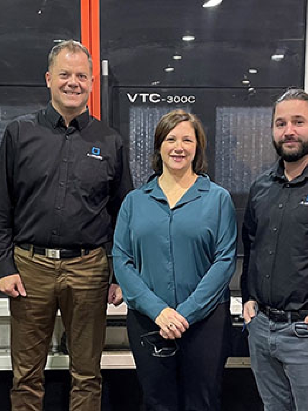 Quatre personnes debout dans un atelier industriel devant une grande machine-outil, posant pour une photo officielle.