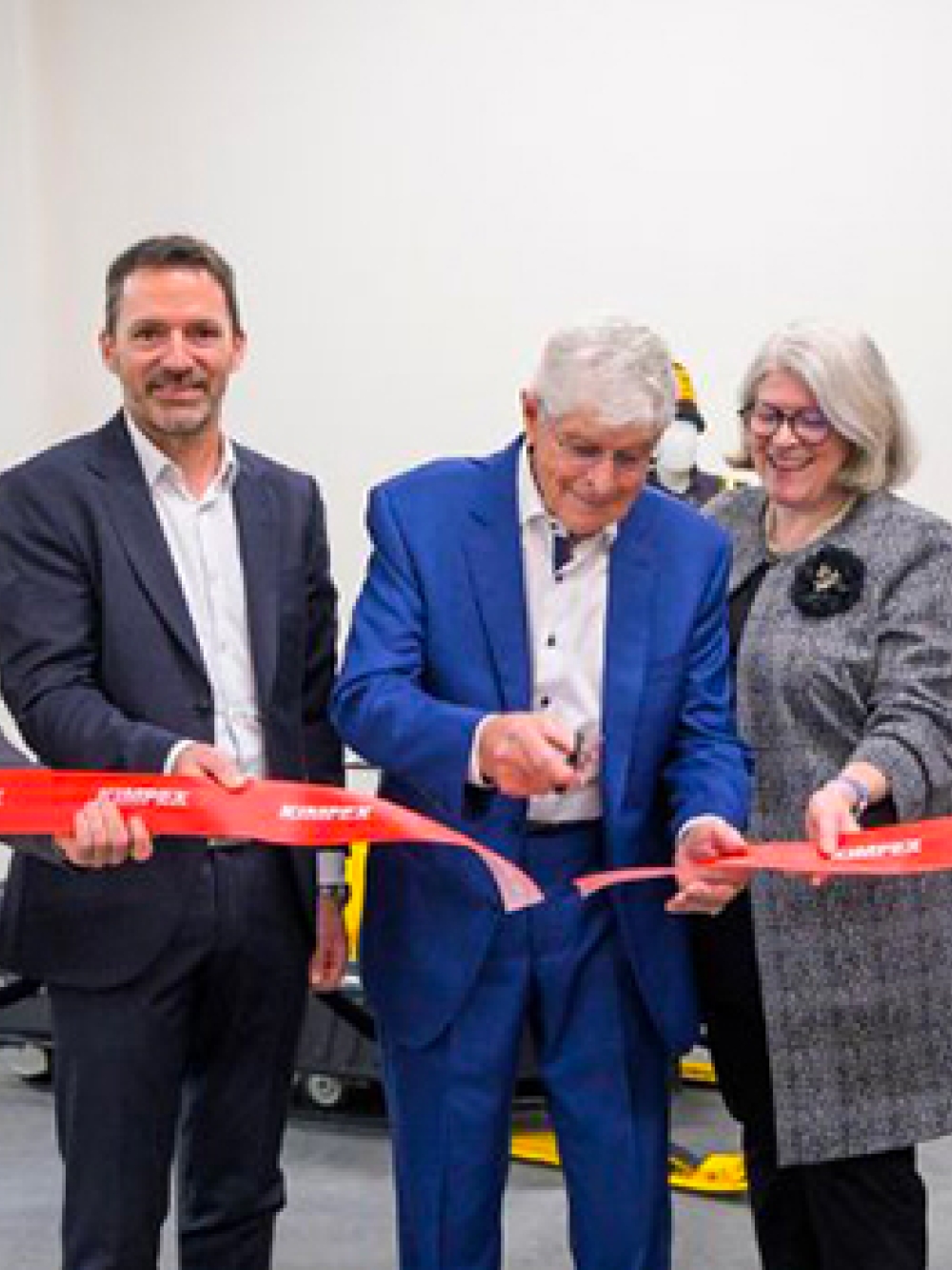 Groupe de personnes participant à une cérémonie d’inauguration et tenant un ruban rouge pendant qu’un homme au centre procède à la coupe.