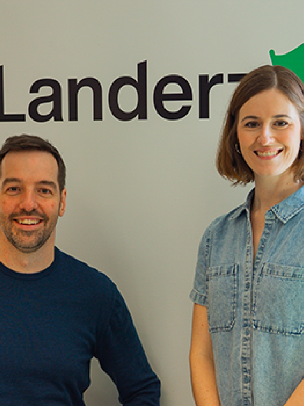 Deux personnes posant dans un bureau devant un mur affichant le logo de Landerz.