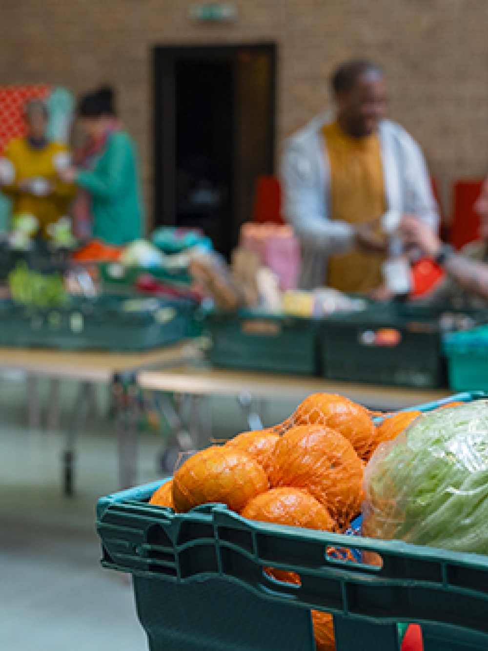  Bacs remplis de fruits et légumes frais dans une salle où des personnes préparent et distribuent des denrées alimentaires.
