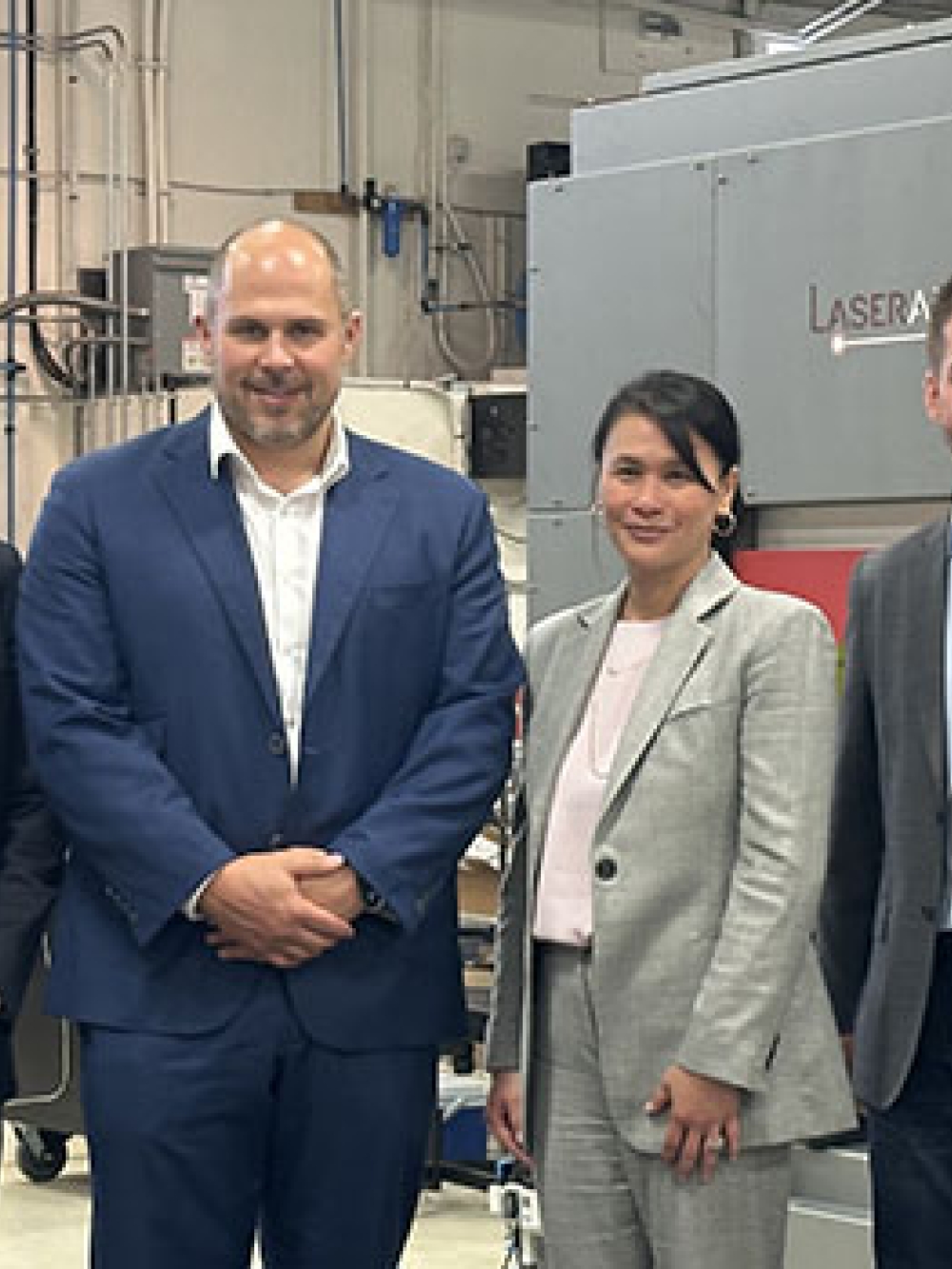 Groupe de personnes debout dans un atelier industriel devant un large équipement portant la marque Laserax, avec des étagères et du matériel technique en arrière‑plan.