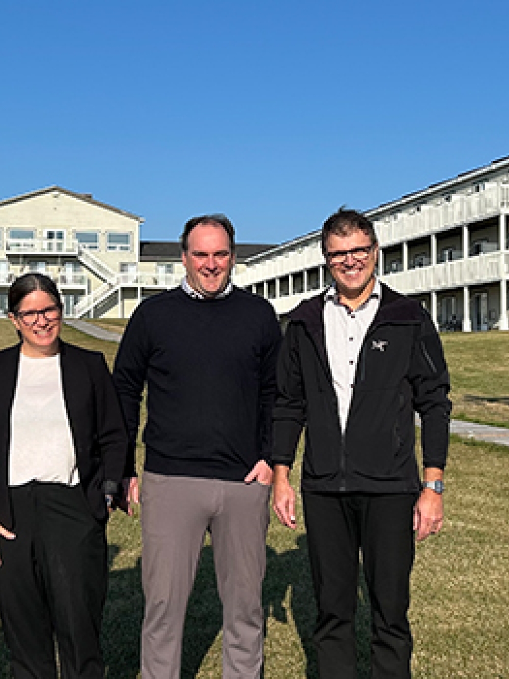 Quatre personnes debout sur une pelouse devant les bâtiments du complexe hôtelier, par une journée ensoleillée.