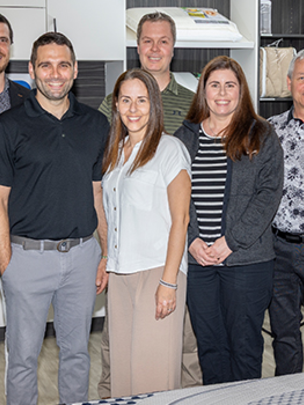 Groupe de personnes posant dans une salle d’exposition de matelas et d’oreillers, entourées d’étalages et de produits de literie.