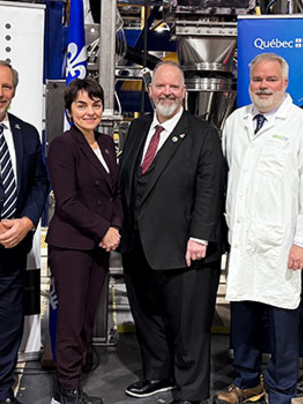 Groupe de personnes debout dans une usine, posant devant des bannières de l’entreprise et du gouvernement du Québec lors d’un événement officiel.