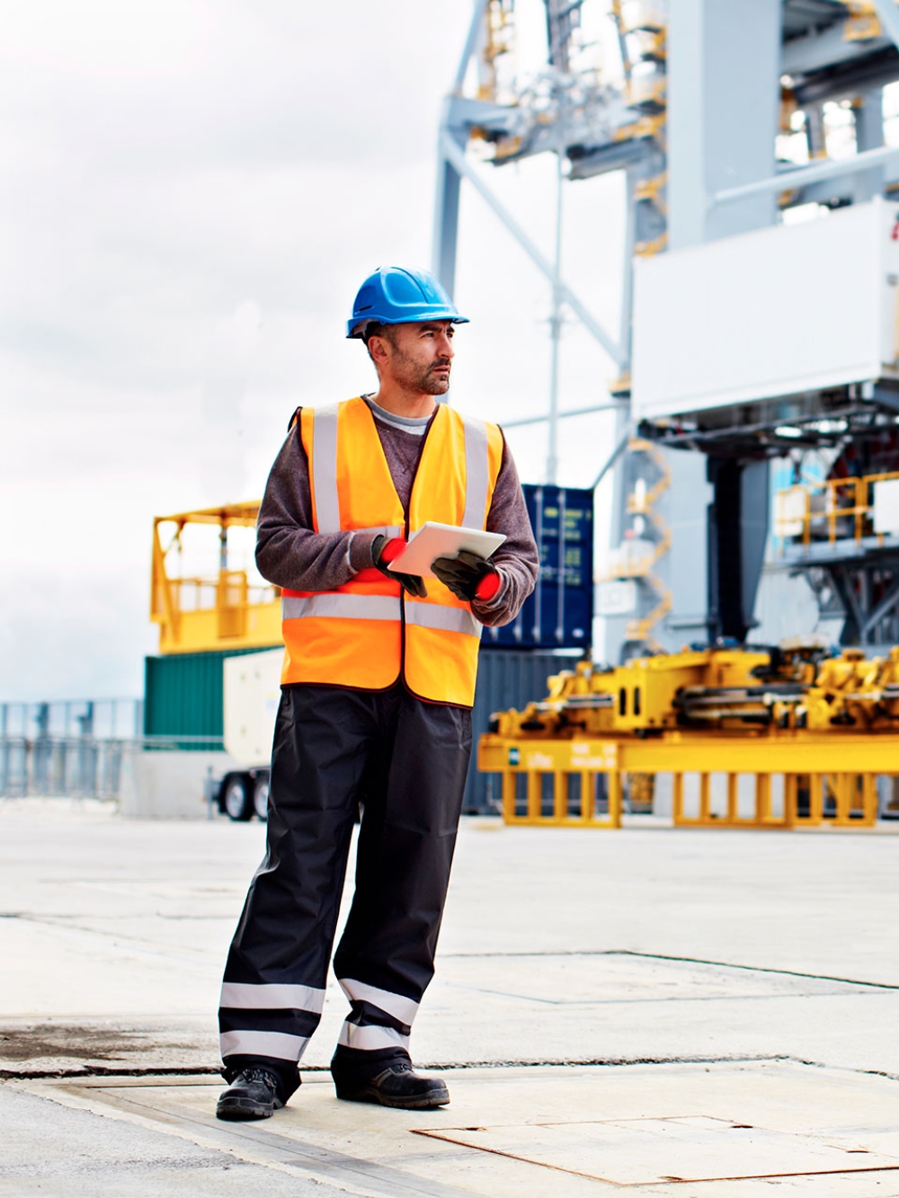 Un employé d'un port tient une tablette entre ses mains près d'un bateau de cargaison