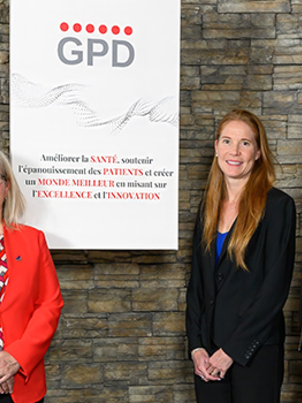 Groupe de personnes debout devant un mur de pierre, posant à côté d’une affiche du Groupe pharmaceutique Duchesnay portant le logo GPD.