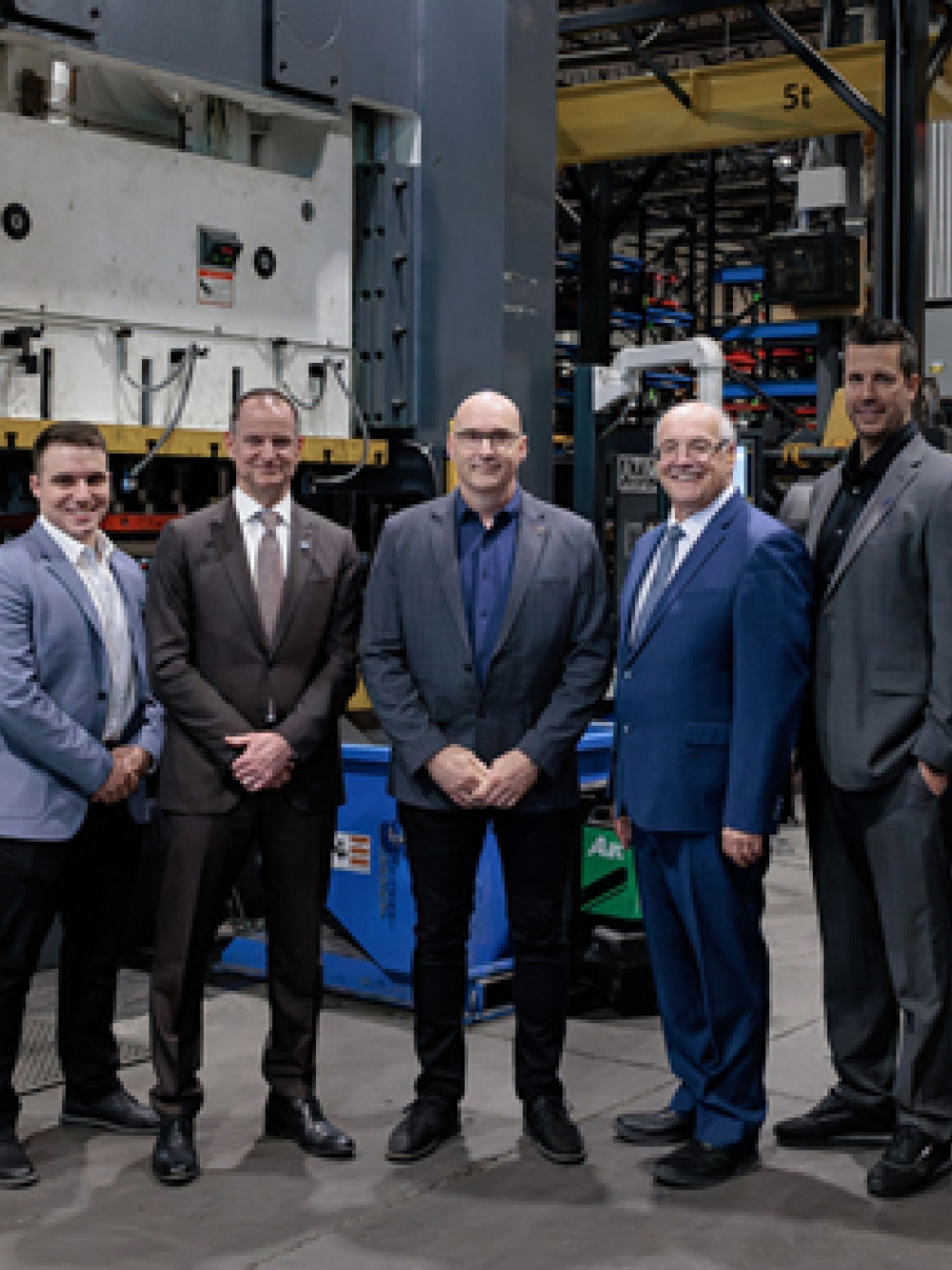 Groupe de personnes debout dans une usine, posant devant un grand équipement industriel entouré de matériel de production et de rayonnages métalliques.
