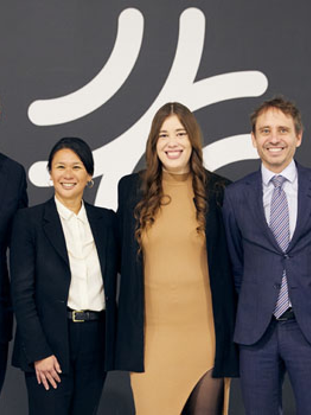 Groupe de cinq personnes debout devant un mur sombre affichant un grand logo blanc.