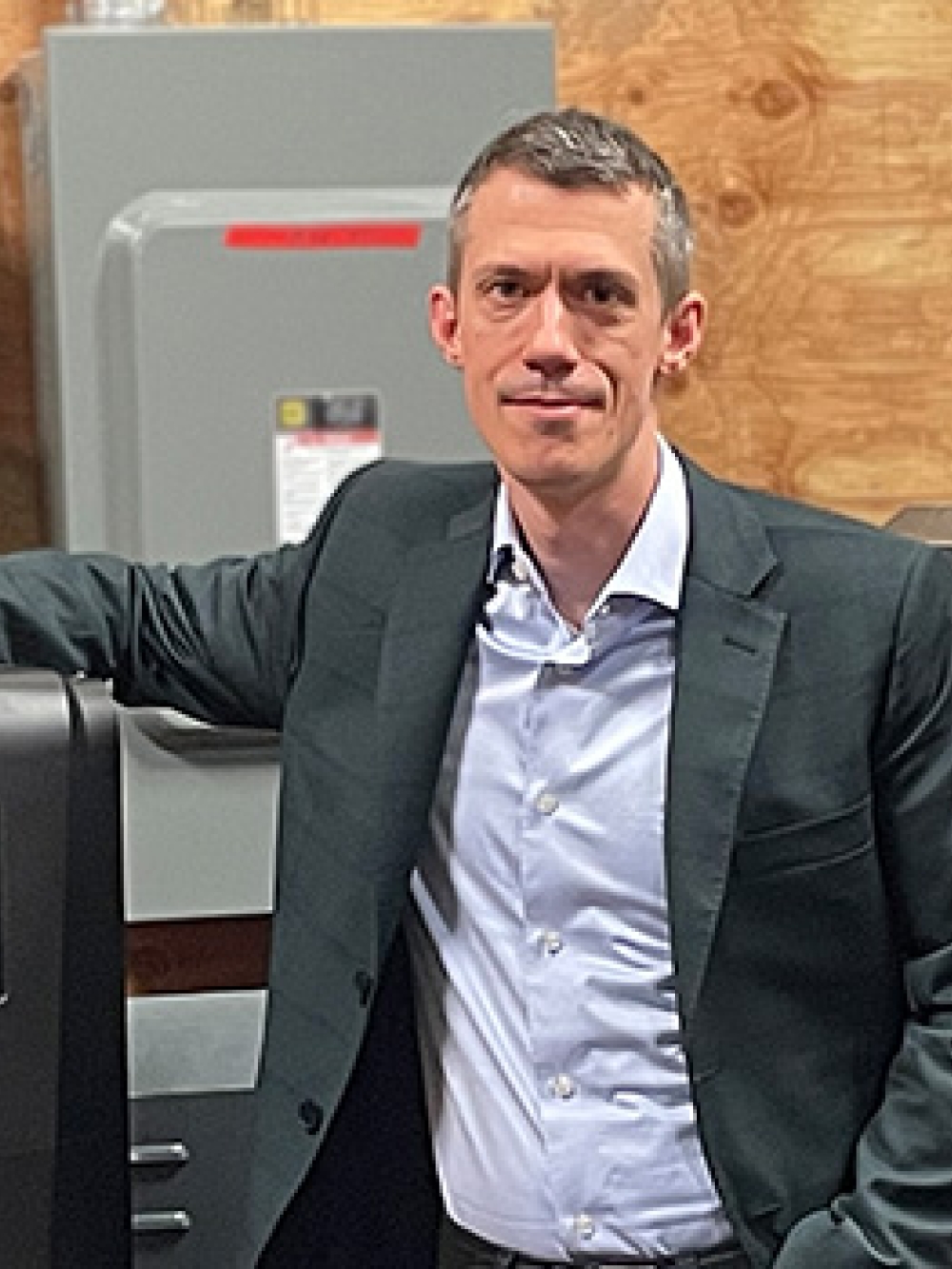 Personne debout dans un atelier industriel, posant à côté d’un équipement électrique et de machinerie. 