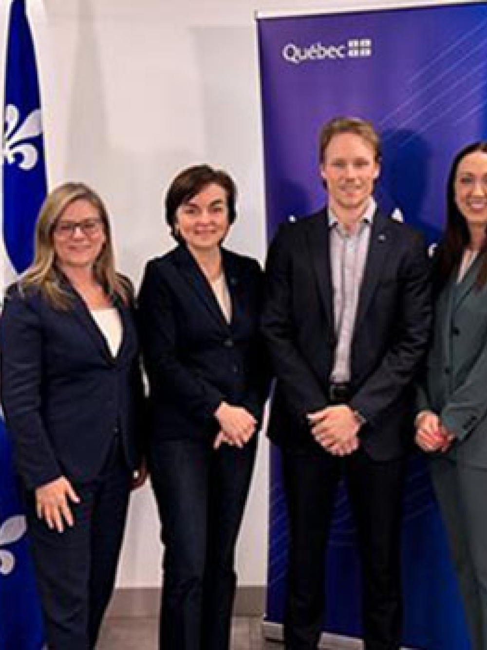 Groupe de personnes debout devant une bannière du gouvernement du Québec et un drapeau fleurdelisé dans une salle intérieure.