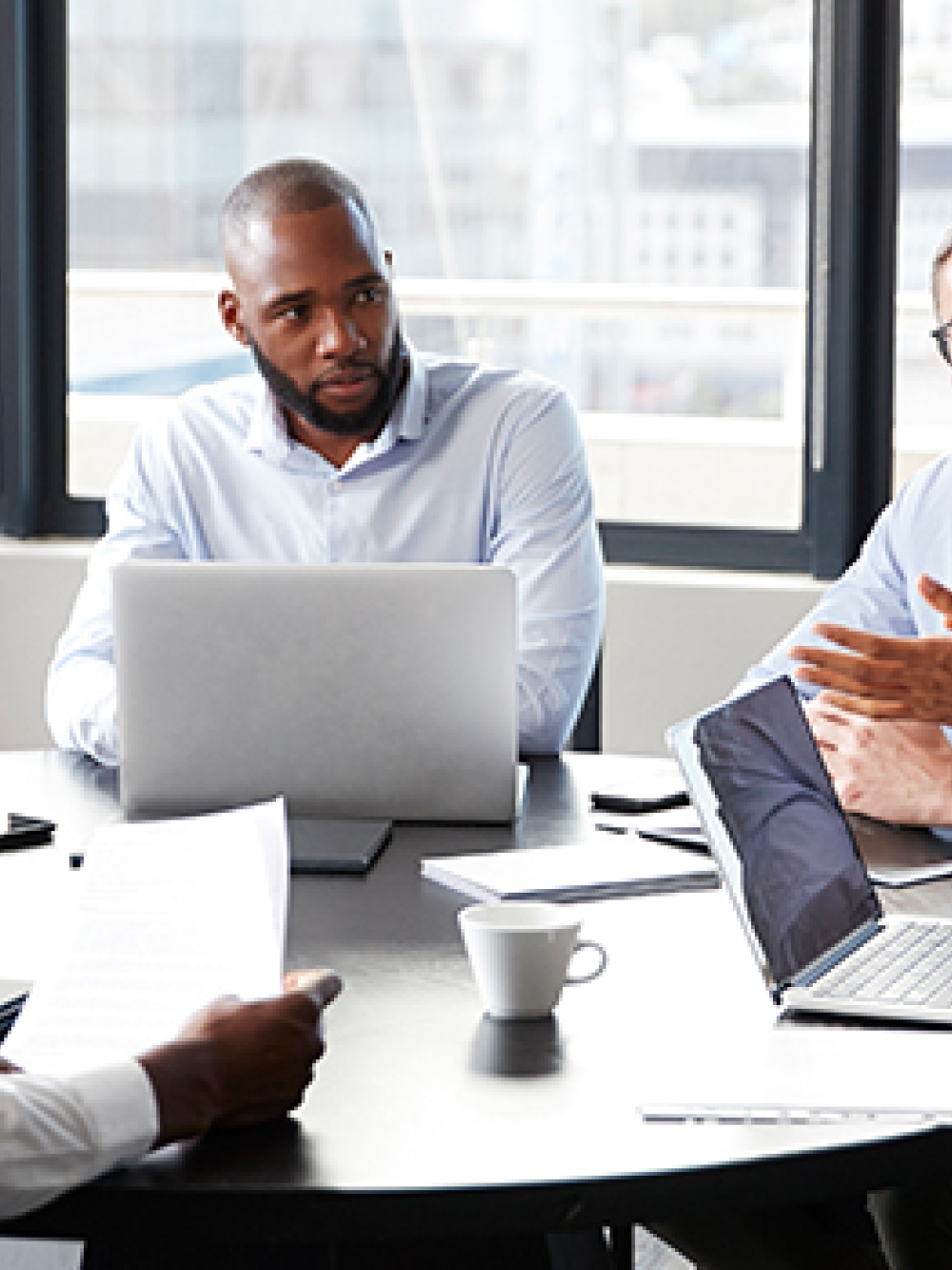 Réunion de travail autour d’une table, où plusieurs personnes échangent et utilisent des ordinateurs portables dans une salle de conférence lumineuse.
