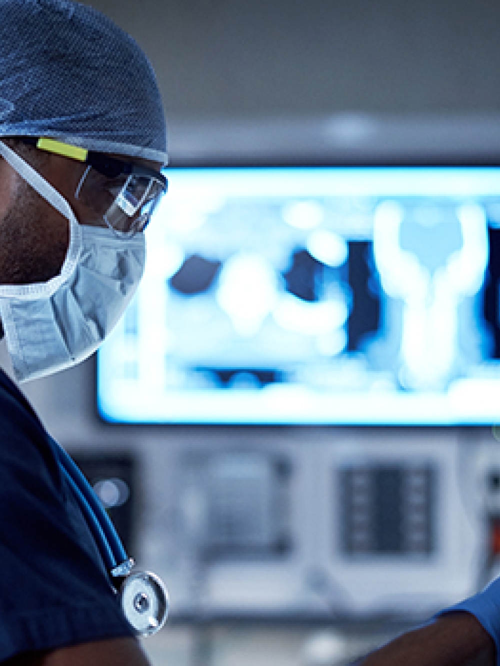 Un professionnel de la santé en salle d’opération utilise des appareils médicaux, avec un écran affichant des images radiologiques. 