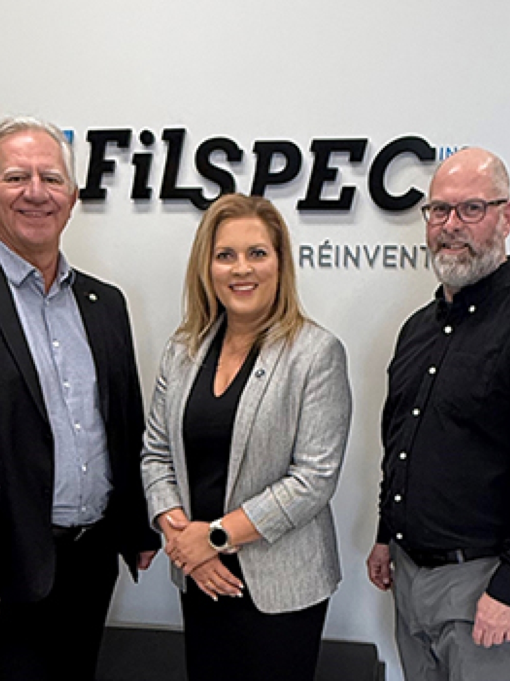 Groupe de personnes debout devant un mur portant le logo de FilSpec, dans un espace d’accueil d’entreprise.