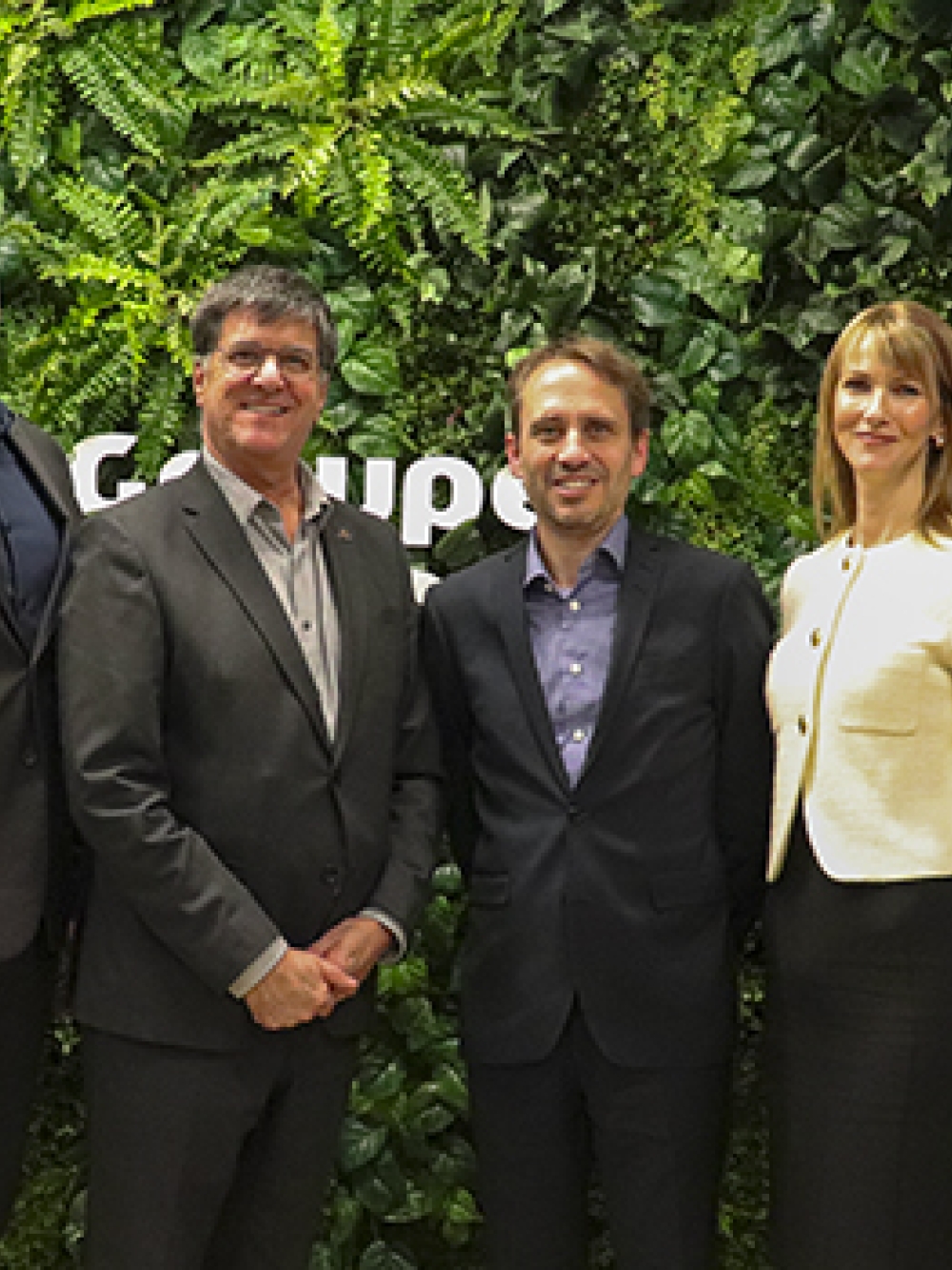Quatre personnes debout devant un mur végétal, encadrées par deux bannières promotionnelles.