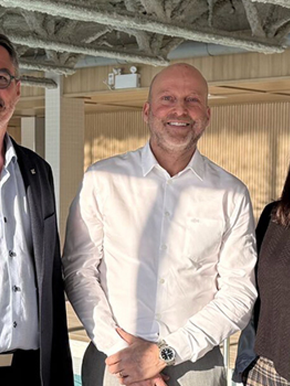 Trois personnes se tiennent dans une zone rénovée de l’hôtel entourée de matériaux en bois et d’un aménagement moderne. 