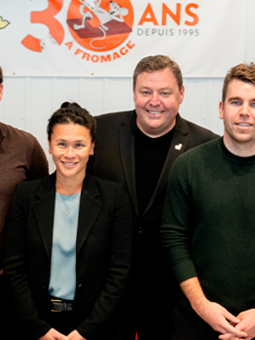 Groupe de personnes posant à l’intérieur d’un commerce, devant une bannière du 30e anniversaire de La Trappe à Fromage et des étagères remplies de produits.
