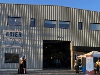 Façade d’une usine moderne en tôle métallique avec le logo « Acier DM » sur le mur, grande porte ouverte.