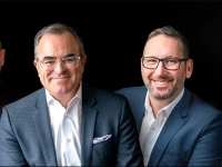 Quatre personnes en tenue professionnelle portant des vestons et chemises blanches, posant devant un fond noir.