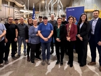 Groupe de personnes debout dans une usine, devant des équipements industriels et une bannière du gouvernement du Québec.