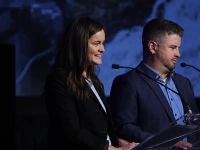 Deux personnes en tenue professionnelle debout derrière un lutrin, parlant devant des micros. 