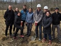 Groupe de personnes debout à l’extérieur dans un milieu naturel, tenant des pelles lors d’une pelletée de terre symbolique sur un terrain boisé.