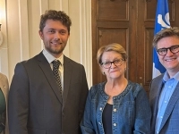 Quatre personnes debout à l’intérieur d’une salle officielle.