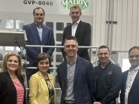 Groupe de personnes posant ensemble dans une usine devant un grand équipement industriel matricé, dans un environnement de production.