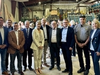 Groupe de personnes debout à l’intérieur d’une scierie, entourées de machines industrielles et d’équipements de production de bois.
