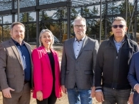 Groupe de personnes debout sur un chantier devant une structure métallique en construction, avec des poutres d’acier et des équipements de chantier visibles en arrière-plan.