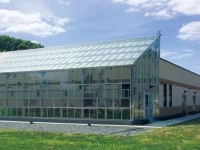 Bâtiment industriel moderne avec une grande serre vitrée à l’avant, situé sur un terrain gazonné, avec un réservoir blanc portant le logo « WaterHub » en arrière-plan.