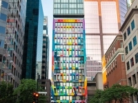 Façade d’un immeuble étroit aux fenêtres colorées au centre-ville, entouré de gratte‑ciel aux tons gris et vitrés.