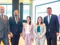Groupe de personnes posant devant une scène lors d’une conférence de presse, avec un écran de présentation et un drapeau du Québec en arrière‑plan.