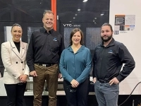 Quatre personnes debout dans un atelier industriel devant une grande machine-outil, posant pour une photo officielle.