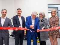 Groupe de personnes participant à une cérémonie d’inauguration et tenant un ruban rouge pendant qu’un homme au centre procède à la coupe.