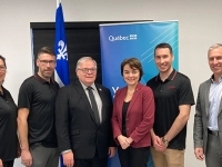 Groupe de personnes posant devant des bannières du gouvernement du Québec, incluant un drapeau fleurdelisé, dans une salle de présentation.
