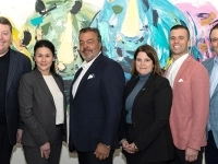 Groupe de personnes en tenue professionnelle posant devant une grande œuvre abstraite colorée dans une salle intérieure.