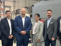 Groupe de personnes debout dans un atelier industriel devant un large équipement portant la marque Laserax, avec des étagères et du matériel technique en arrière‑plan.