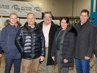 Groupe de personnes debout dans un entrepôt industriel, vêtues de manteaux d’hiver, posant devant des structures métalliques et du matériel de scierie.