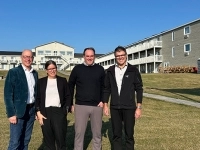 Quatre personnes debout sur une pelouse devant les bâtiments du complexe hôtelier, par une journée ensoleillée.