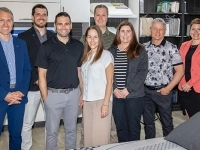 Groupe de personnes posant dans une salle d’exposition de matelas et d’oreillers, entourées d’étalages et de produits de literie.